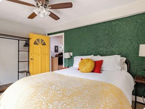 A bedroom with a bed, a ceiling fan, a yellow door, and a green textured wall. - “The Clementine” Boho Home in Orlando’s Food Scene (Orlando)