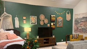 A living room with a bed, TV, green wall, artwork, and a table with chairs. - “The Clementine” Boho Home in Orlando’s Food Scene (Orlando)
