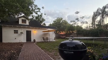 A backyard with a brick pathway leading to a white house, a black grill, and outdoor furniture.