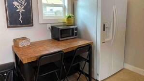 A compact kitchen with a white refrigerator, a microwave, and a wooden table with two chairs. - “The Clementine” Boho Home in Orlando’s Food Scene (Orlando)