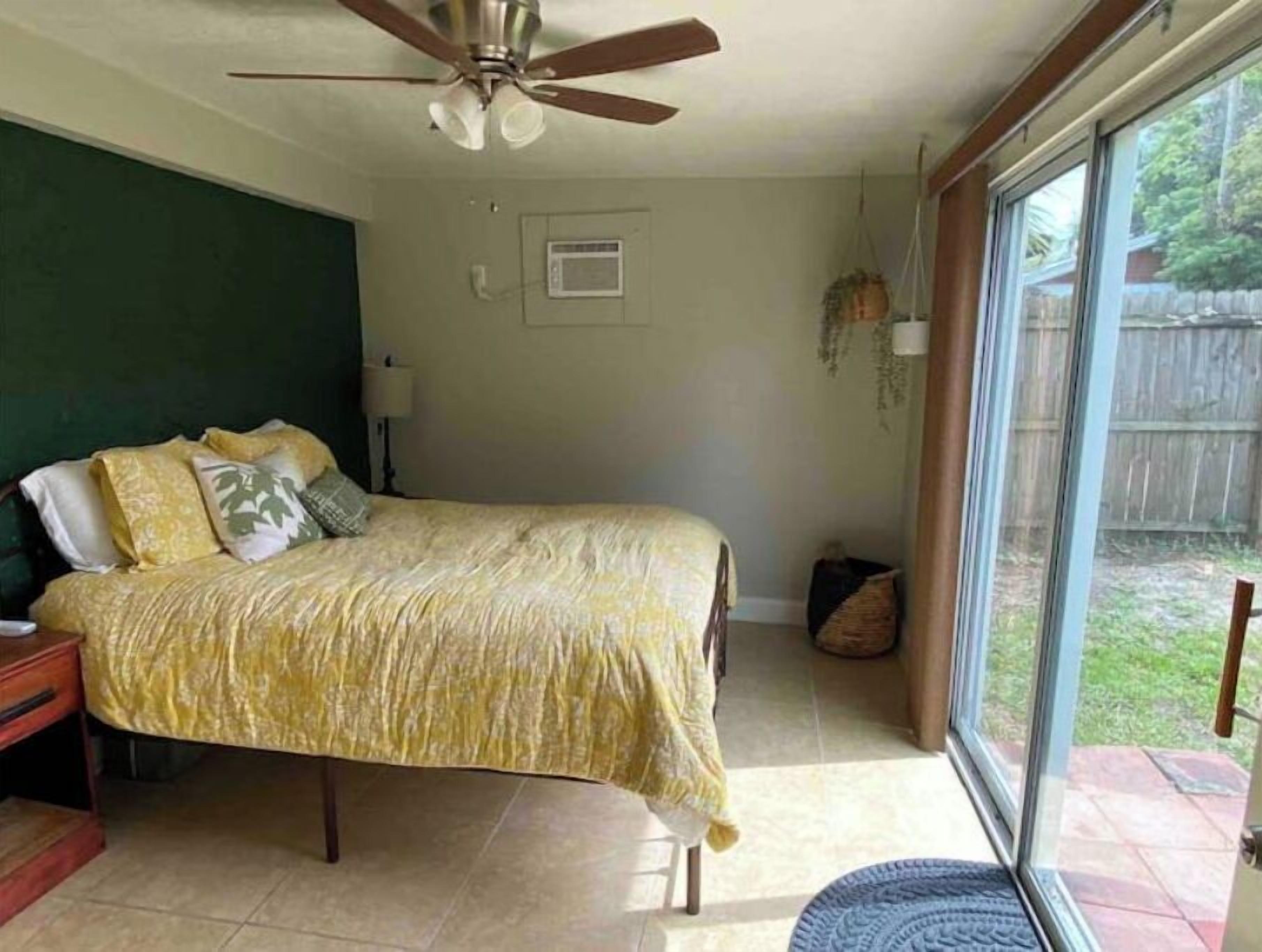 Une chambre à coucher avec un lit, un ventilateur de plafond, une fenêtre et une porte.