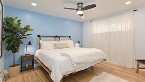 A bedroom with a bed, a ceiling fan, a nightstand, a lamp, a potted plant, and a window with curtains. - Renovated Hidden-Gem Minutes from Downtown Denver with coffee bar (Aurora)