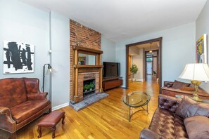 A living room with a brick fireplace, leather sofas, a glass coffee table, and a television.