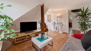 Un salon avec un téléviseur posé sur un meuble en bois, une table basse blanche, un canapé et une grande plante.