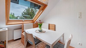 Un coin repas comprenant une table, des chaises, un vase avec des fleurs, une fenêtre donnant sur un paysage agréable et un luminaire suspendu.