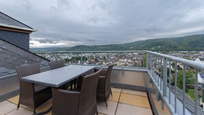Un balcon extérieur avec une table et des chaises, offrant une vue sur le paysage urbain et les collines.