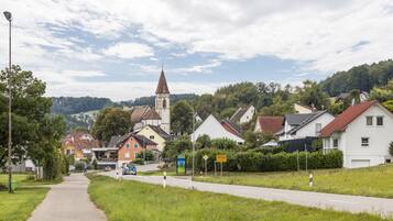 A rural road leading to a village with houses, a church, and a sign indicating a nearby town.