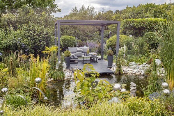 A garden with a gazebo, a pond, and various plants.