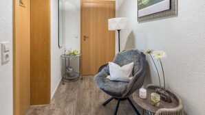 A room with a wooden door, a grey armchair with a pillow, a small table with a lamp, and a wall-mounted picture. - Deluxe Apartment 'Griesbaum' with Private Terrace, Shared Garden and Wi-Fi (Tengen-Büßlingen)