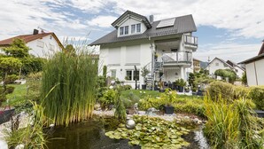 A two-story house with a garden pond, surrounded by various plants and trees. - Deluxe Apartment 'Griesbaum' with Private Terrace, Shared Garden and Wi-Fi (Tengen-Büßlingen)