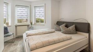 A modern bedroom with a bed, two windows with blinds, a chair, and a radiator. - Deluxe Apartment 'Griesbaum' with Private Terrace, Shared Garden and Wi-Fi (Tengen-Büßlingen)