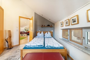 Une chambre à coucher avec un lit, un banc, une sculpture en bois et une fenêtre avec des stores.