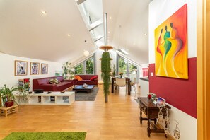 A spacious living area with a red sofa, a coffee table, and a dining table. There are potted plants and artwork on the walls. - Charming 70 sqm Holiday Apartment with Wi-Fi by Christine van Impelen (Passau)