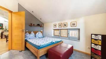 Ein Schlafzimmer mit einem Bett, einer roten Bank, einer Holztür, einem Regal mit Gegenständen sowie einer Wand mit gerahmten Bildern und Nummernschildern.