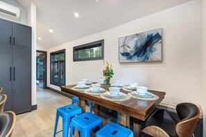 Un coin repas avec une longue table dressée pour le repas, des chaises bleues et une peinture abstraite moderne accrochée au mur.
