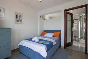 A bedroom with a bed, a dresser, a framed picture, and a bathroom with a shower. - Seafront Adriatic Pearl Suite, Kraljevica, Croatia (Kraljevica)