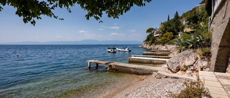 A pebble beach with boats, clear water, and a rocky shoreline.
