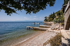 A pebble beach with boats, clear water, and a rocky shoreline. - Seafront Adriatic Pearl Suite, Kraljevica, Croatia (Kraljevica)