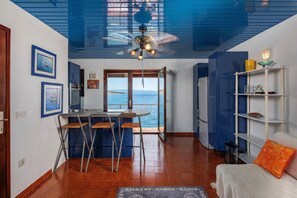 A room with a view of the sea, a ceiling fan, a dining area, and a white sofa.