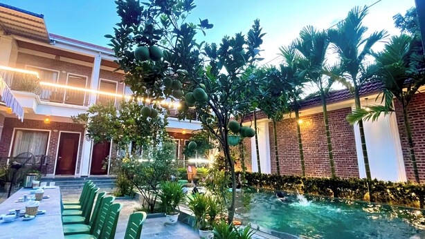 A pool area with a dining table and chairs, surrounded by greenery and a brick building. - Mai Mountain Homestay (Nam Hoa Lu)