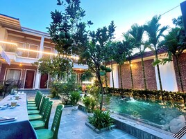 Zona de piscina con mesa y sillas, rodeada de vegetación y un edificio de ladrillo.