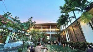 A courtyard with a pool, palm trees, and a building with a balcony. - Mai Mountain Homestay (Nam Hoa Lu)