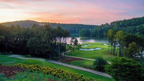 A golf course with a lake, surrounded by trees and a sunset sky. - Mai Mountain Homestay (Nam Hoa Lu)
