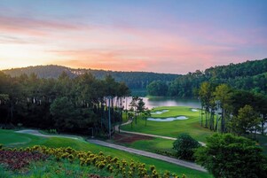 Campo de golf con un lago, rodeado de árboles y un cielo al atardecer.