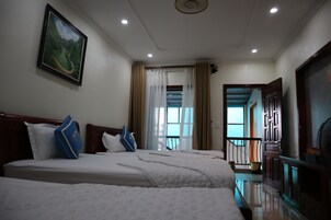 Habitación de hotel con dos camas, un cuadro en la pared, vistas a través de la ventana y una puerta que da a un balcón.
