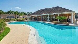 Une piscine dotée de chaises longues et d’un espace abrité, le tout entouré de bâtiments en briques.