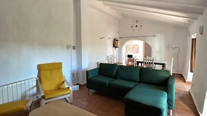 A living room with a green sectional sofa, a yellow armchair, and a wooden coffee table. There is a dining area in the background with a table and chairs. - Burruelo Ranch in Algodonales (Algodonales)