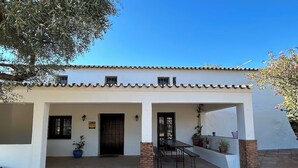 A building with a tiled roof, a central entrance with a door, and a patio area with a table and chairs. - Burruelo Ranch in Algodonales (Algodonales)
