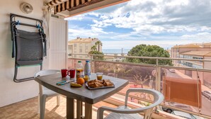 A balcony with a table set for breakfast, a chair, and a view of the sea and buildings. - Studio Apartment 'Les Ptits Loups, Le Grau D'agde' with Sea View and Air Conditioning (Agde)
