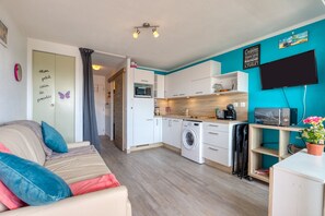 A compact living space with a kitchenette, a sofa with cushions, a washing machine, and a flat-screen TV mounted on the wall. - Studio Apartment 'Les Ptits Loups, Le Grau D'agde' with Sea View and Air Conditioning (Agde)