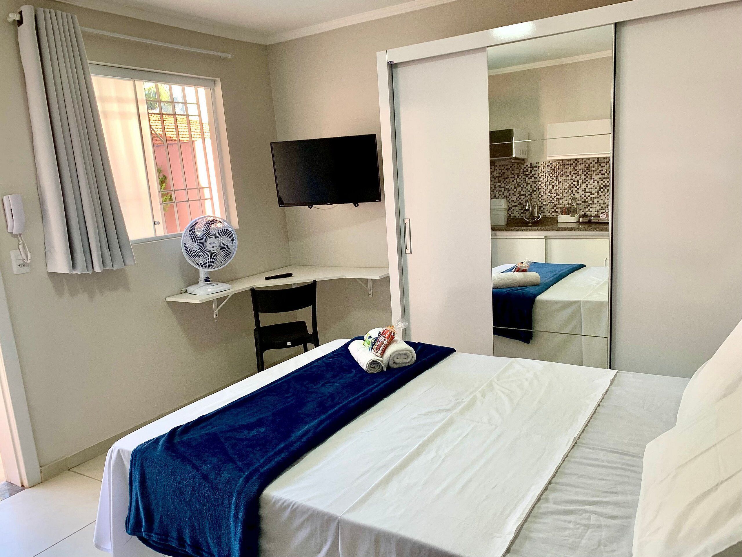 Habitación de hotel con una cama, un escritorio con silla, televisión y un baño visible en un espejo.