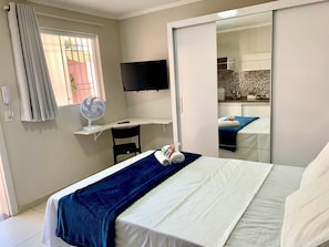 Habitación de hotel con una cama, un escritorio con silla, televisión y un baño visible en un espejo.