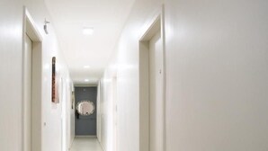 A long, narrow hallway with white walls and doors on both sides, leading to a room with a large mirror on the wall. -  Vila Nina (São Paulo)