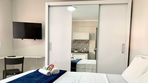 A hotel room with a bed, a desk, a chair, a TV, and a bathroom visible through an open door. -  Vila Nina (São Paulo)