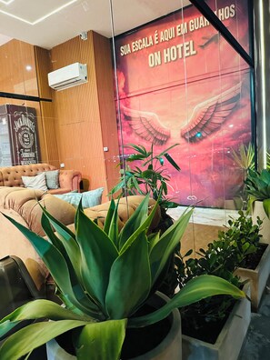 A hotel lobby with a large wall mural, a seating area with sofas, and potted plants. - On Park Hotel Translado e Café da manhã (Guarulhos)