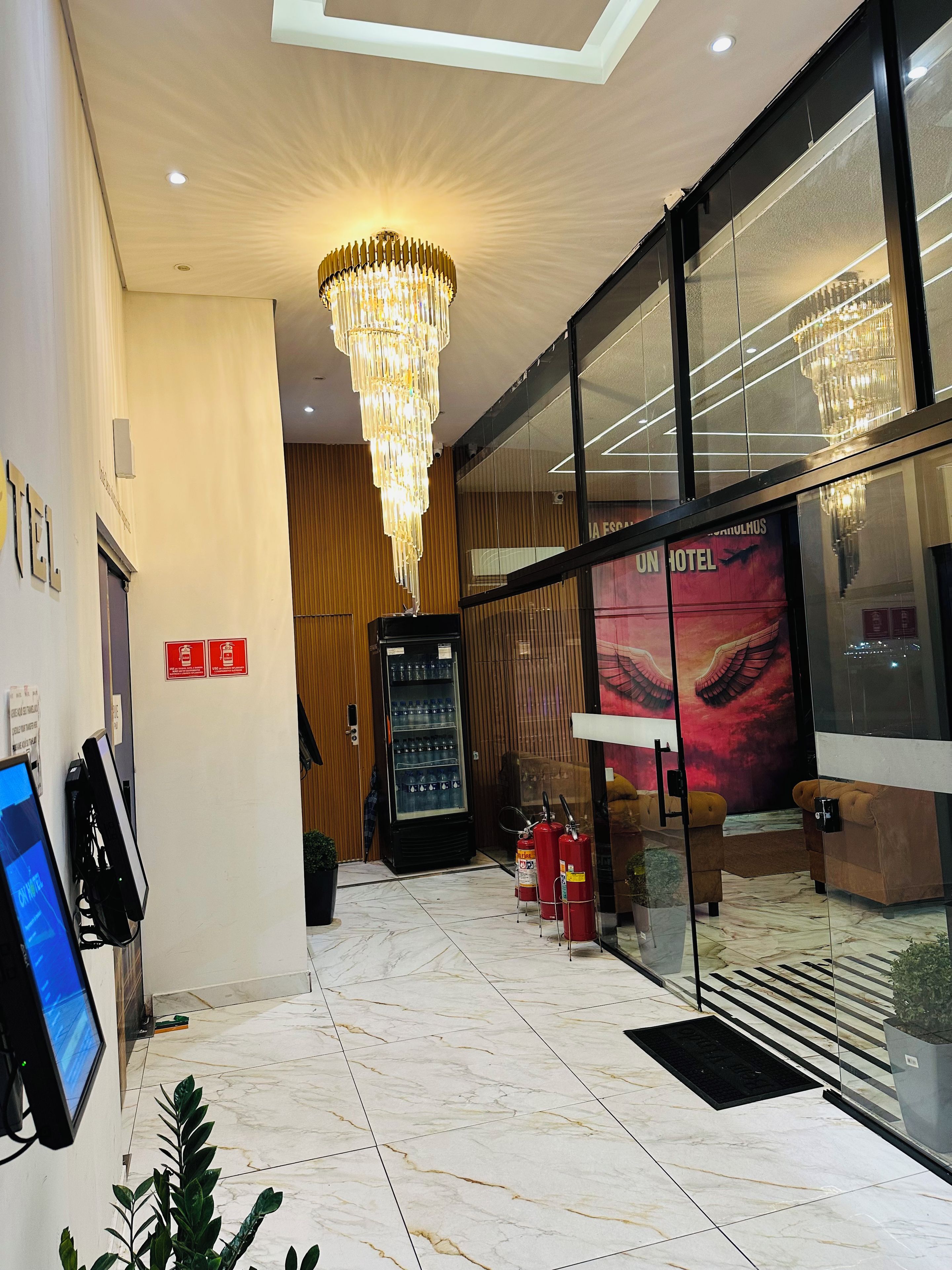 A hotel lobby with a modern chandelier, a digital information kiosk, and a glass wall with a view of the interior.