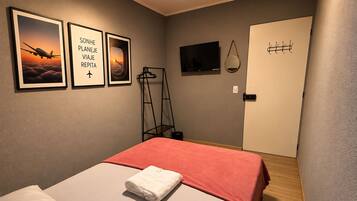 A hotel room with a bed, a TV, a door, and three framed pictures on the wall.