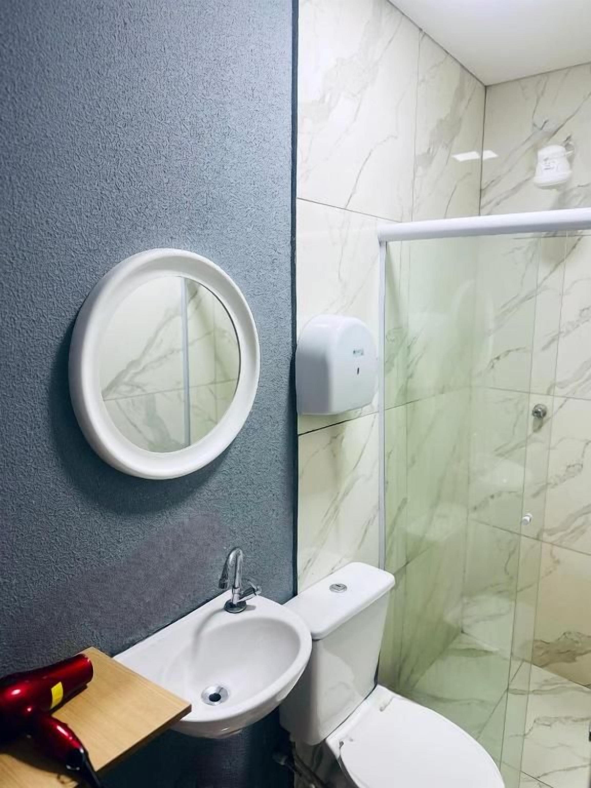 Un baño con lavamanos, espejo, inodoro y cabina de ducha con mampara de vidrio.