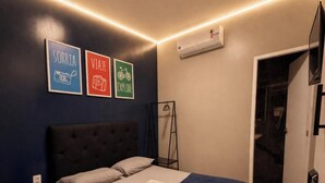 Een slaapkamer met een bed, een nachtkastje, een wandairconditioner en drie ingelijste motiverende posters.