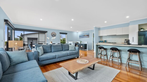 Ein modernes Wohnzimmer mit einem blauen Sofa, einem Holztisch und einer Küche mit weißen Schränken sowie einer Bar.