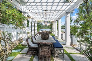An outdoor patio with a long dining table, wicker chairs, and a pergola overhead. - Gorgeous, Peaceful Sanctuary on lake minutes from Boston & all local colleges. (Wayland)