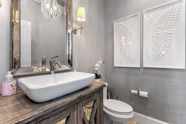 A bathroom with a large mirror, a white sink, a chandelier, and two framed wall art pieces. - Gorgeous, Peaceful Sanctuary on lake minutes from Boston & all local colleges. (Wayland)
