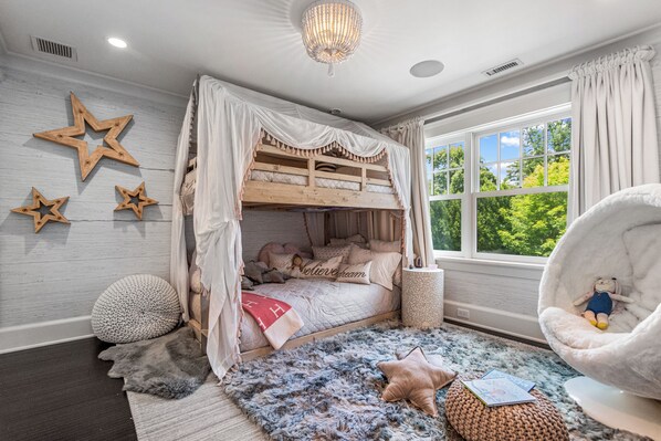 Un dormitorio acogedor con literas, adornos de estrellas, un sillón mullido y vistas al exterior.