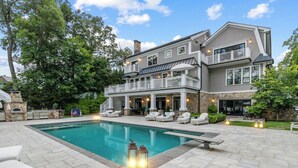 Une grande maison avec une piscine, un espace salon extérieur et une cheminée en pierre.