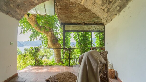 Un balcón con vistas a un lago y montañas, una silla de mimbre y un árbol grande.
