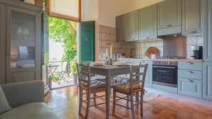 Una cocina con armarios verde claro, una mesa de comedor para cuatro personas y un ventanal con vistas a la vegetación.
